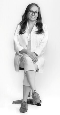 A black-and-white portrait of female dentist Dr. Oksana Bailey sitting on a chair